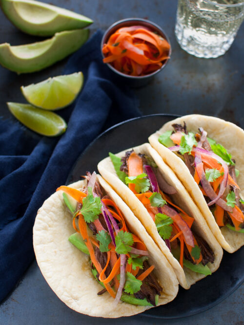 Three Korean beef tacos on a black plate.