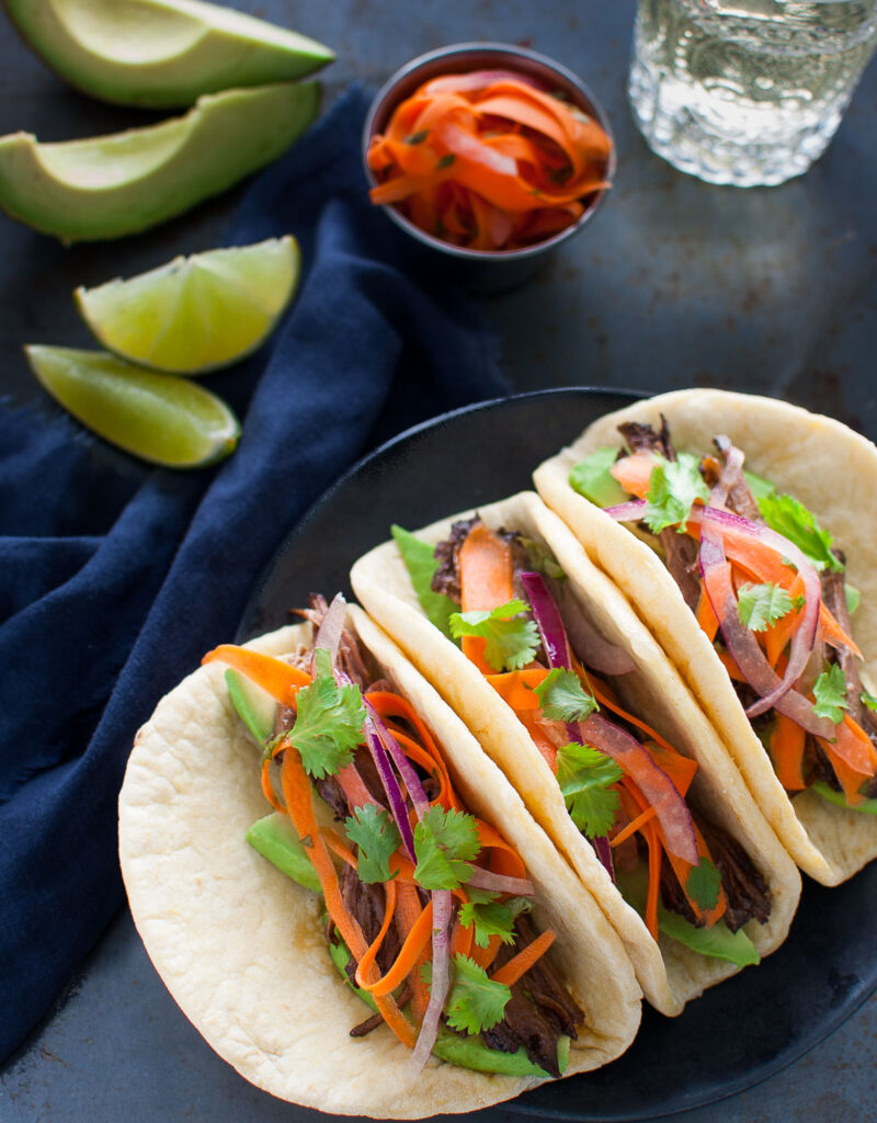 Three Korean beef tacos on a black plate.